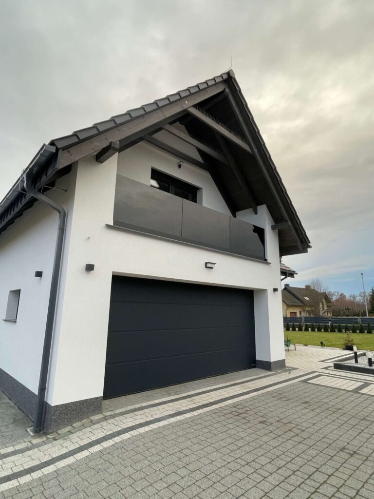 Balkon nad bramą garażową ze szklaną balustradą, dom jednorodzinny z białą elewacją