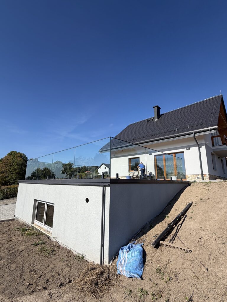 Dom jednorodzinny z tarasem na dachu parterowej części, otoczonym balustradą ze szkła