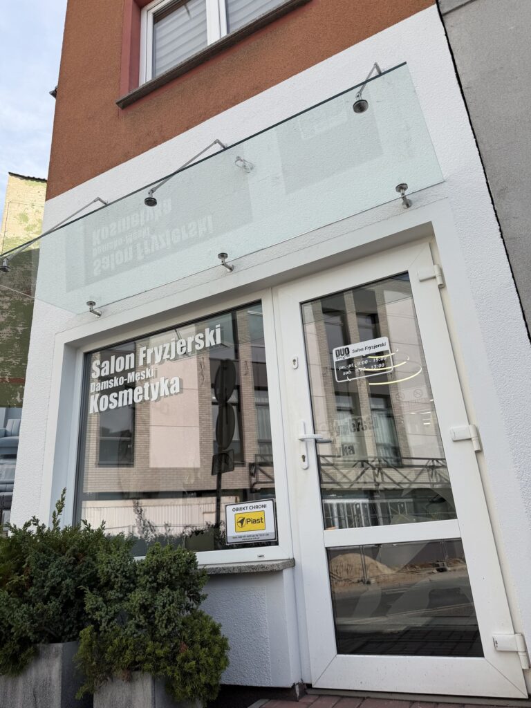 Szklany daszek na cięgnach nierdzewnych nad wejściem do salonu fryzjerskiego