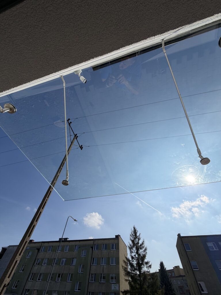 Tafla szklanego daszku widziana od spodu, mocowanie punktowe i cięgna nierdzewne