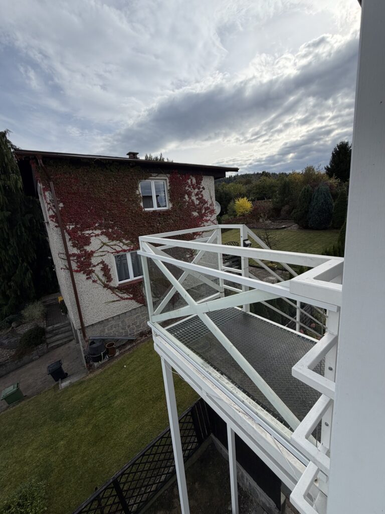 Stalowy pomost na piętrze z balustradą wypełnioną szkłem i białymi krzyżulcami