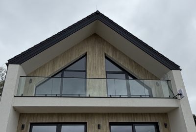 Nowoczesny dom z dwuspadowym dachem i balkonem na całą szerokość ze szklaną balustradą