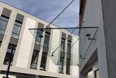 Szklany daszek nad wejściem do lokalu, podwieszony na stalowych cięgnach