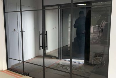 Przyciemniane szklane drzwi dwuskrzydłowe w ścianie z czarnymi poziomymi profilami